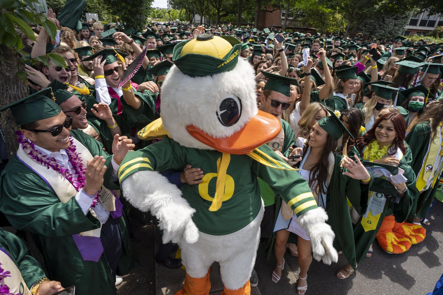 The Duck mascot surround by excited students wearing graduation attire
