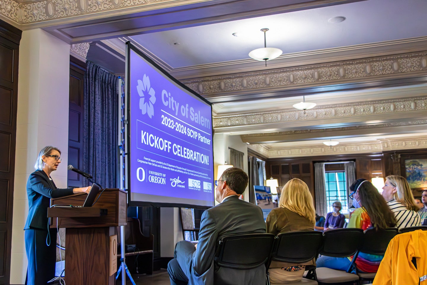 Photograph of Dean Parr talking to a crowded room in Gerlinger Hall, a historic building with furnishings from the early twentieth century. 