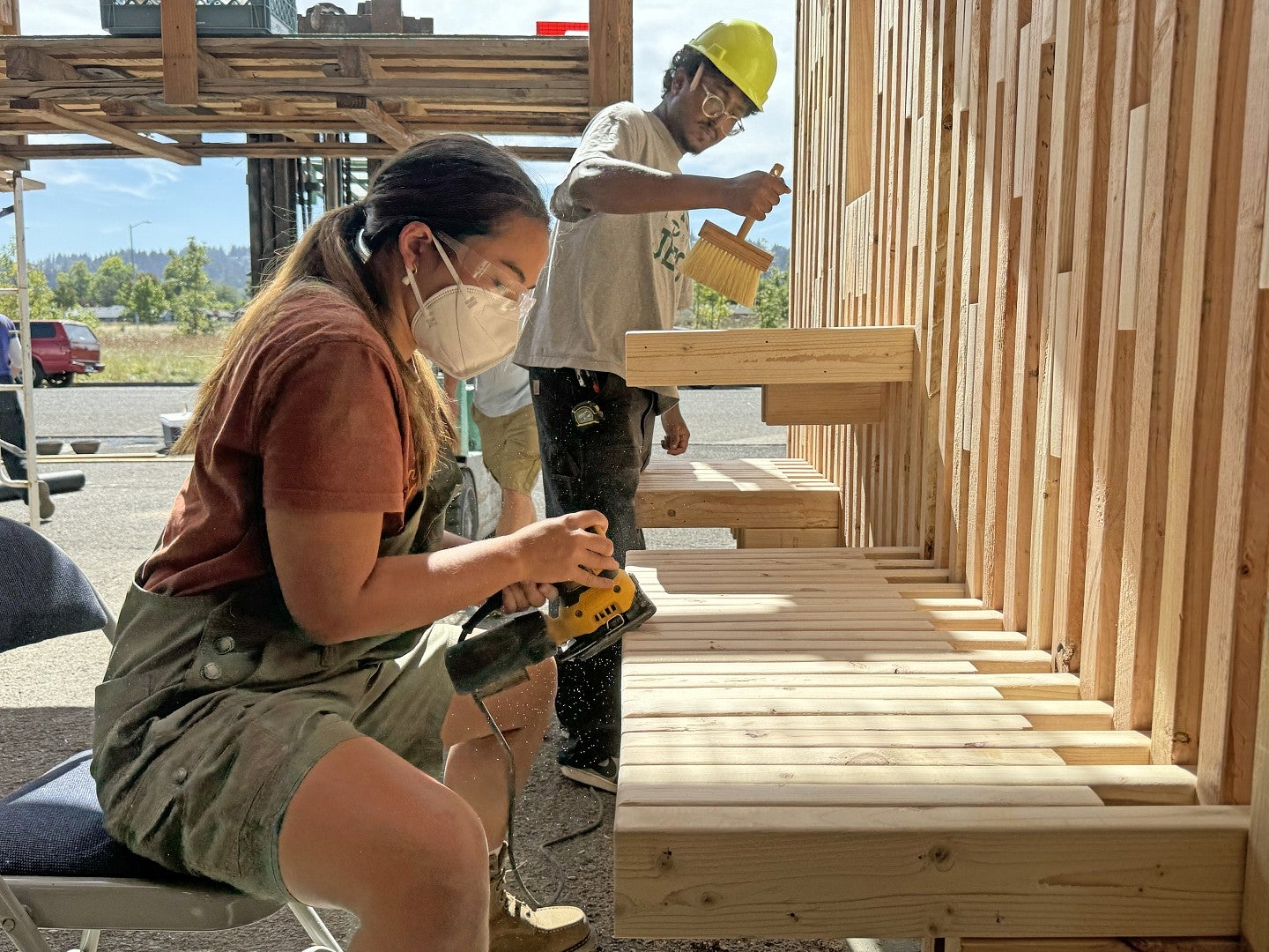 Group shot of a student sanding and another student cleaning lumber.