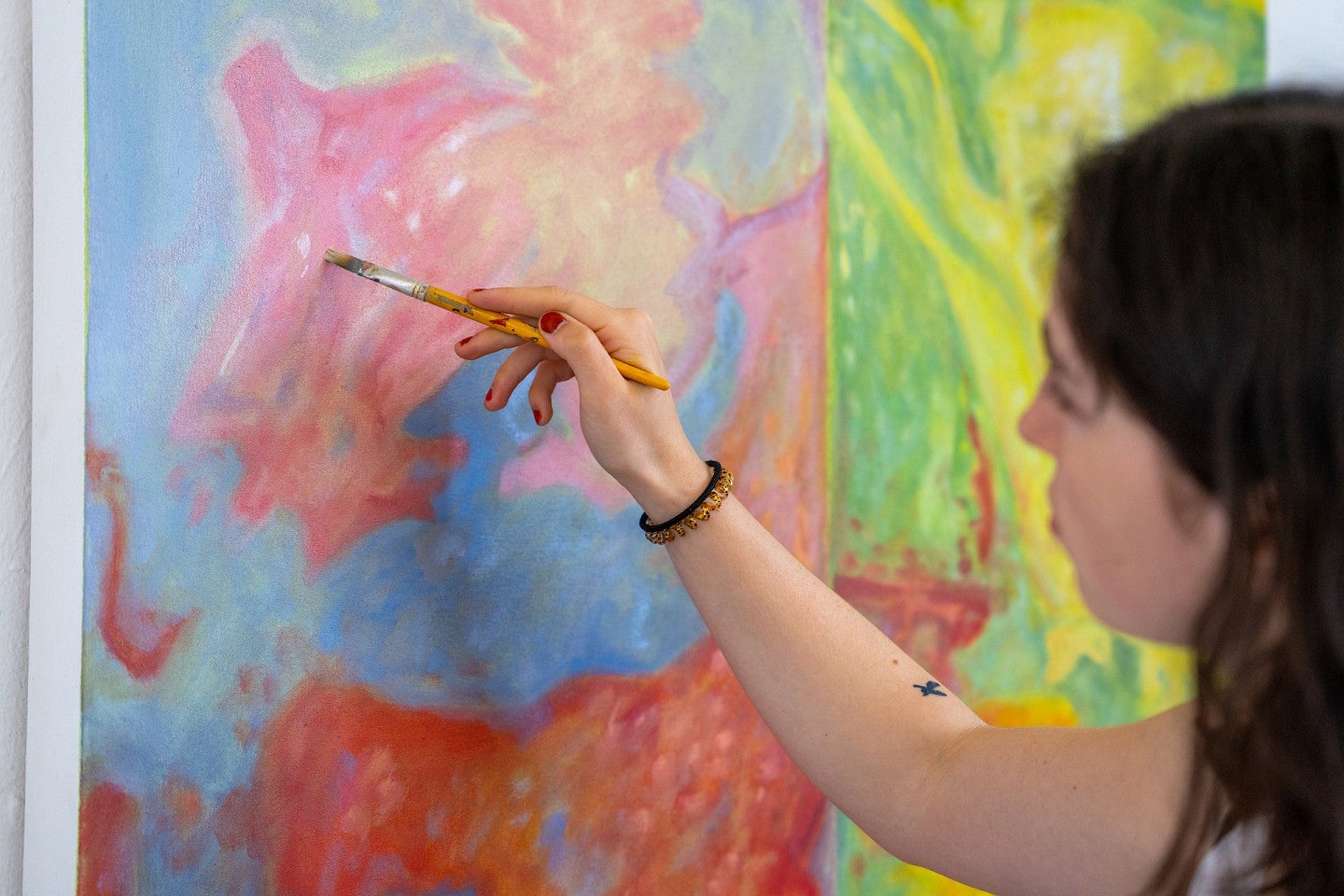 Student painting pink, blue, green, and yellow piece