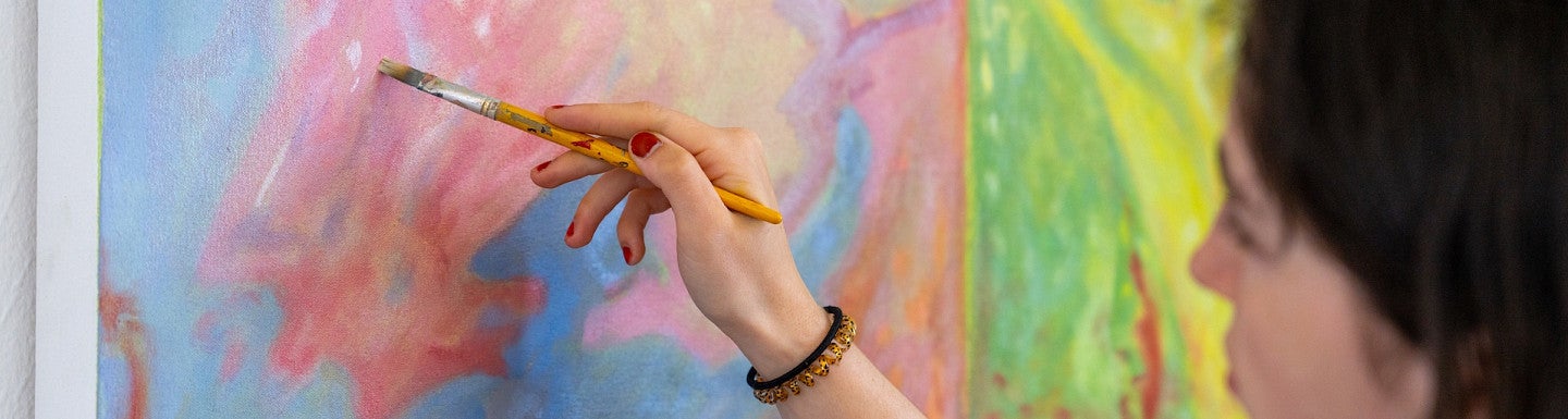 Student painting pink, blue, green, and yellow piece