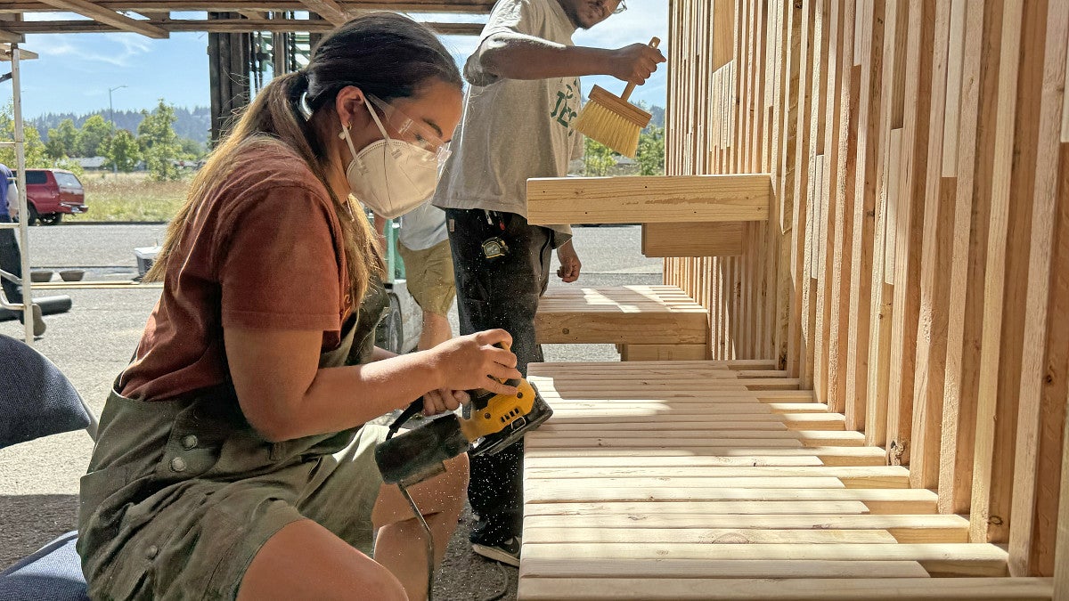 Group shot of a student sanding and another student cleaning lumber.