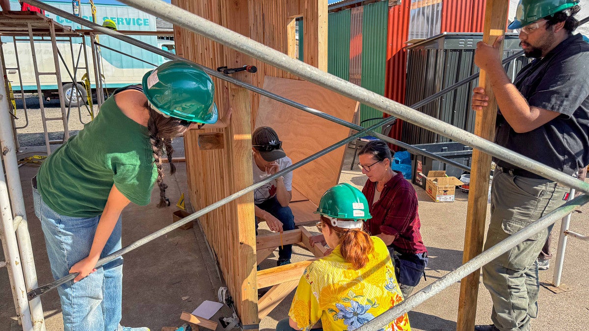 students inspect the outdoor kitchen with hard hats firmly on top of their heads. 
