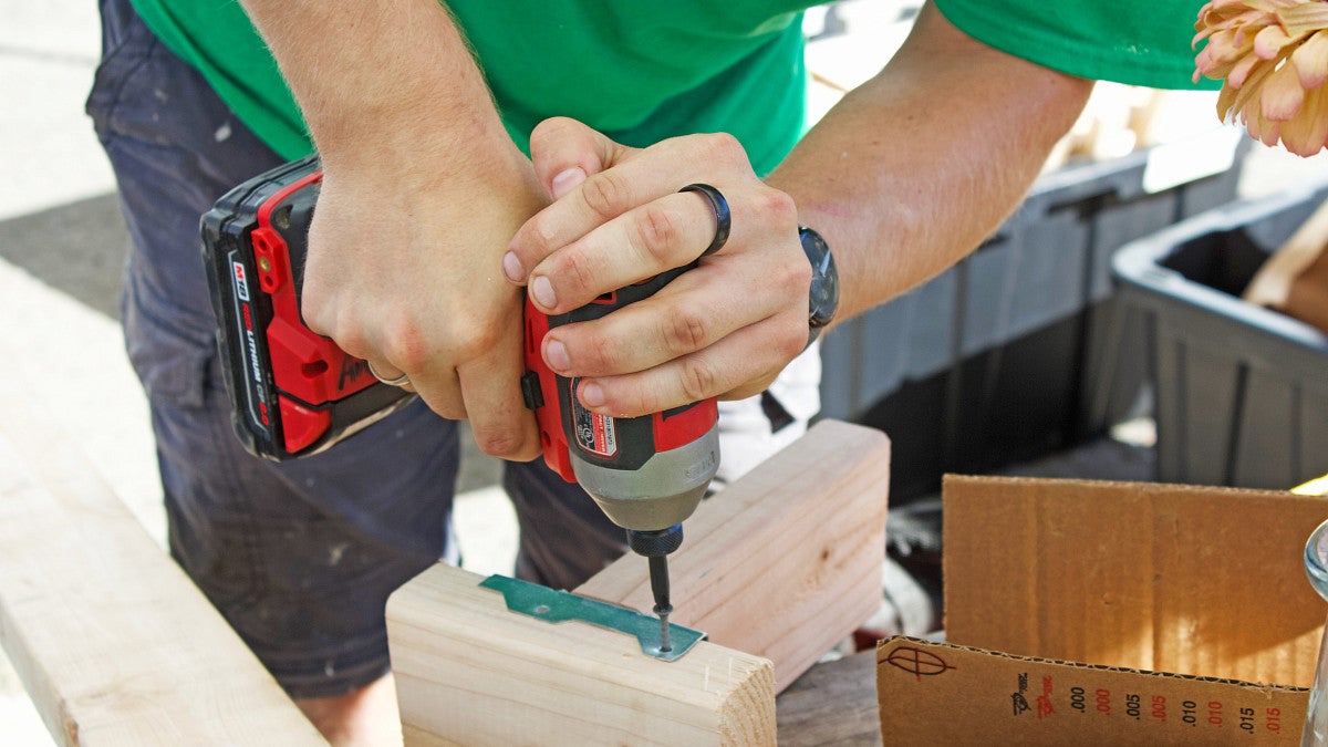 Photograph of a BDI participant using a drill to screw into a metal bracket to join two wood pieces. 