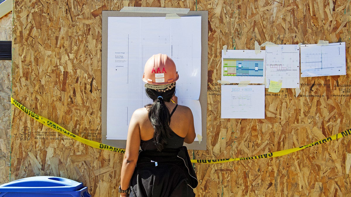 BDI photo of a student in front of a building diagram on a construction site. 