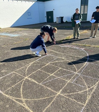 Students drawing geometric symbols outdoors at Sheldon on the blacktop. 