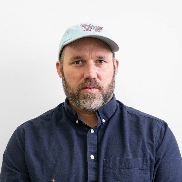 Photograph of a bearded male in a ballcap looking into the camera. 