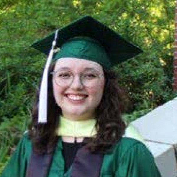 Photograph of a woman in graduation robes and hat smiling into the camera. 
