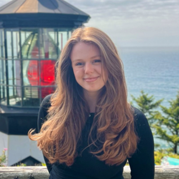 Femme presenting individual smiles into the camera with long hair in front of a historic lighthouse. 