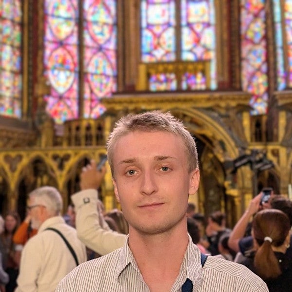 Masc presenting individual looking into the camera in a crowded historic church. 