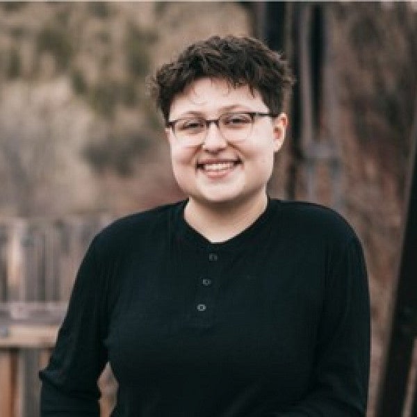 Photograph of an individual smiling into the camera with short hair and glasses. 