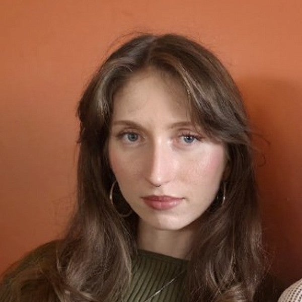 Femme presenting individual looks into the camera in front of a warm colored wall. 