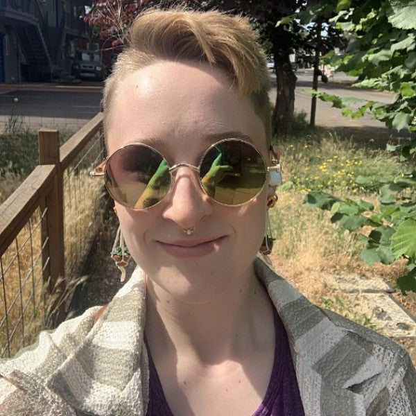 Shows a individual looking into the camera with sunglasses and short hair. 