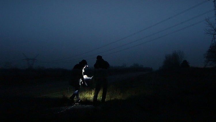 two people in the dark with flashlight in field under power lines