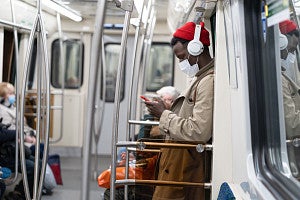 Man on a subway wearing a beanie, headphones, and a protective mask