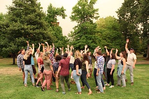 Photo of the latest RARE cohort outdoors with green trees and grass and arms raised in joy. 