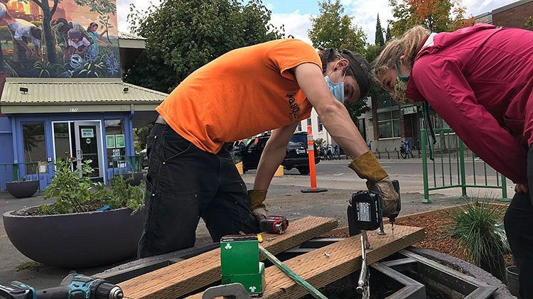 two people assemble metal and wood object