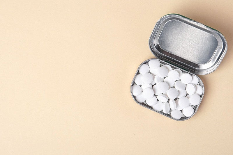 A tin of white mints is displayed on a peach-colored surface.