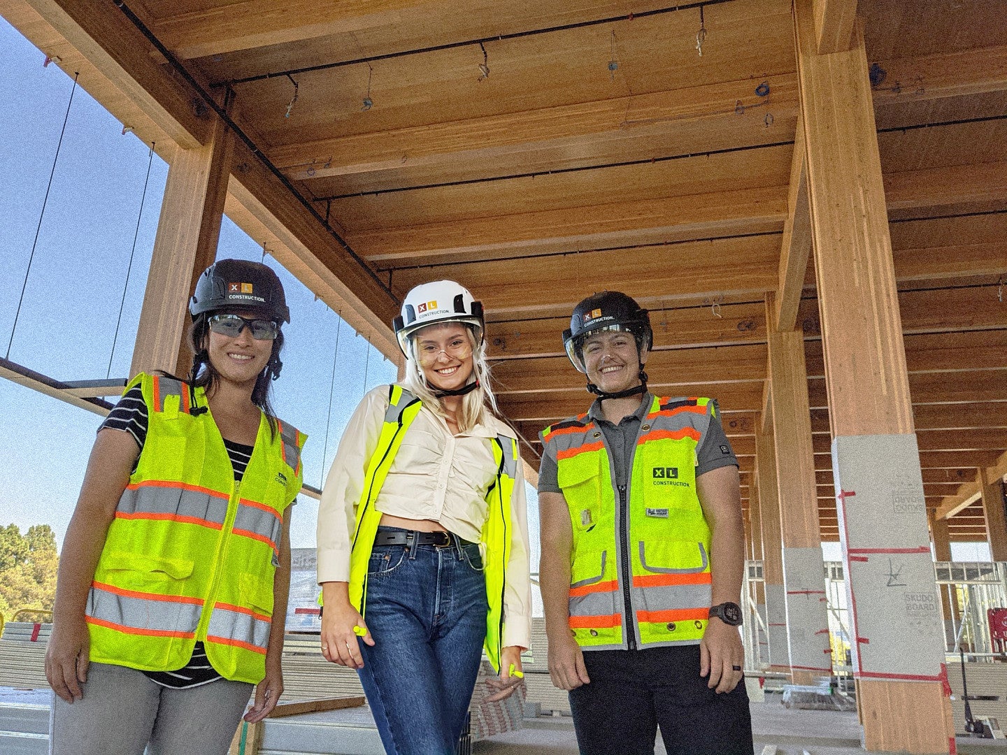 Honour and company posing in hard hats and high-visibility vests in a wooden frame of a building