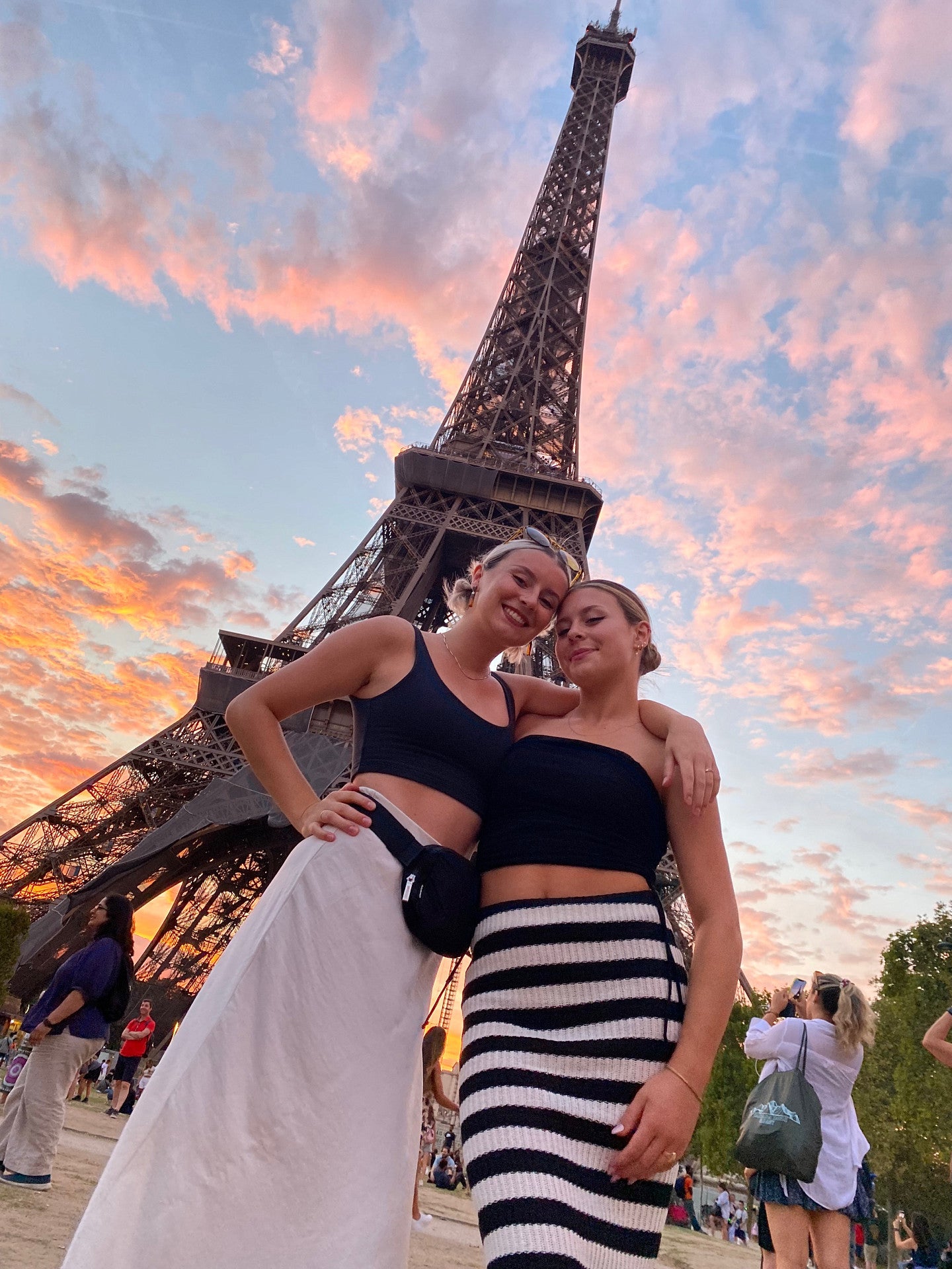 Honour and her friends in front of the Eiffel Tower. The sun is setting, so the clouds in the sky are pink and orange.