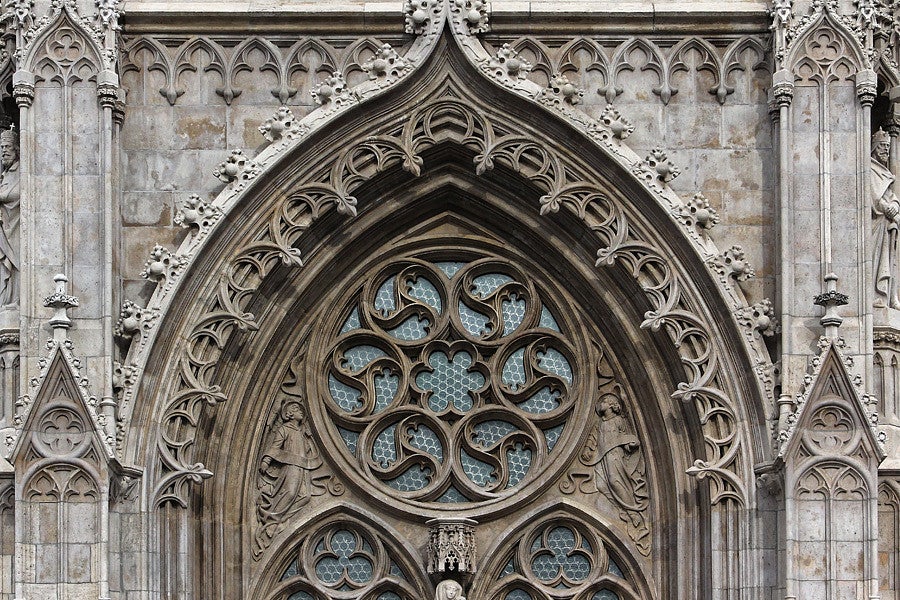 Photograph of Gothic architecture. Exterior view of a church window that show ornate, european-style stone features and glass.
