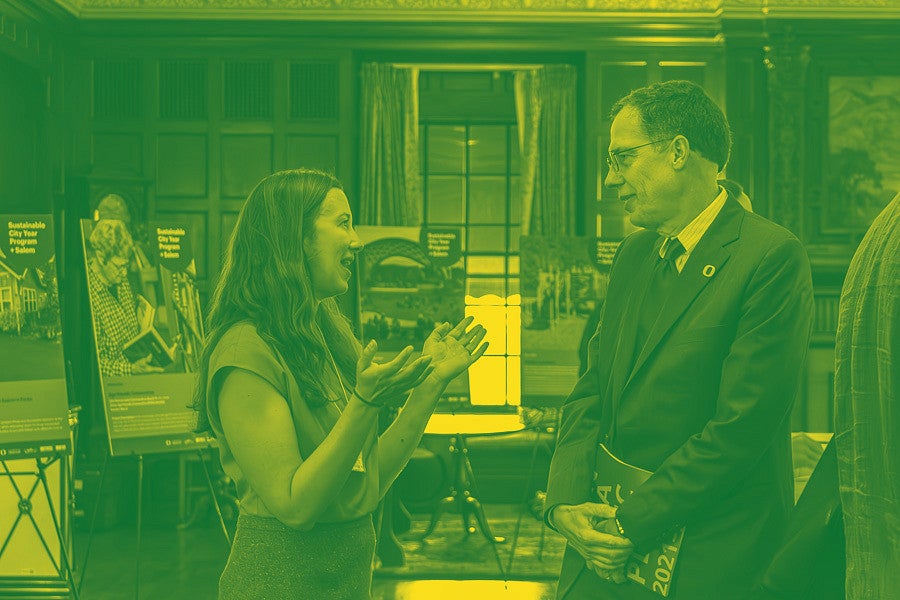 SCYP kick-off photograph showing communication lead, Lindsey Hayward and UO President Karl Scholz talking. Photograph is colored as a duotone in UO green and yellow. 