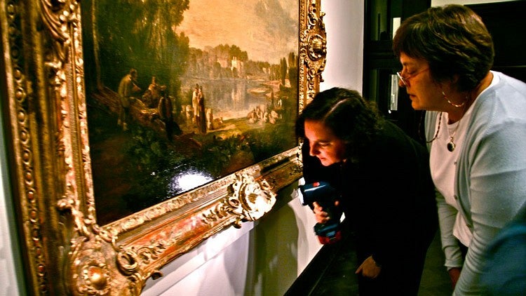 two people inspect framed art at museum with flashlight