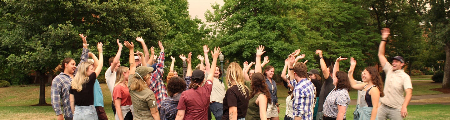 Photo of the latest RARE cohort outdoors with green trees and grass and arms raised in joy. 