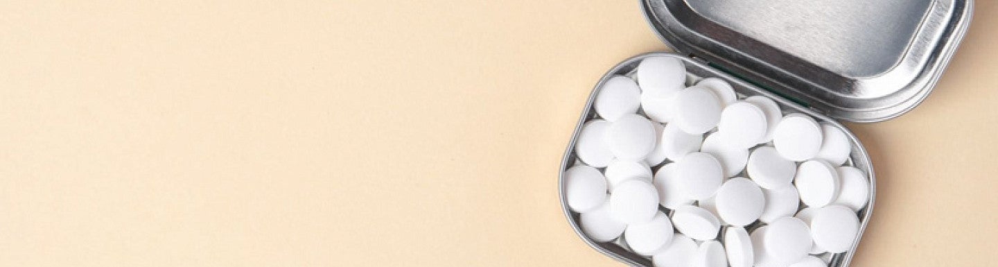 A tin of white mints is displayed on a peach-colored surface.