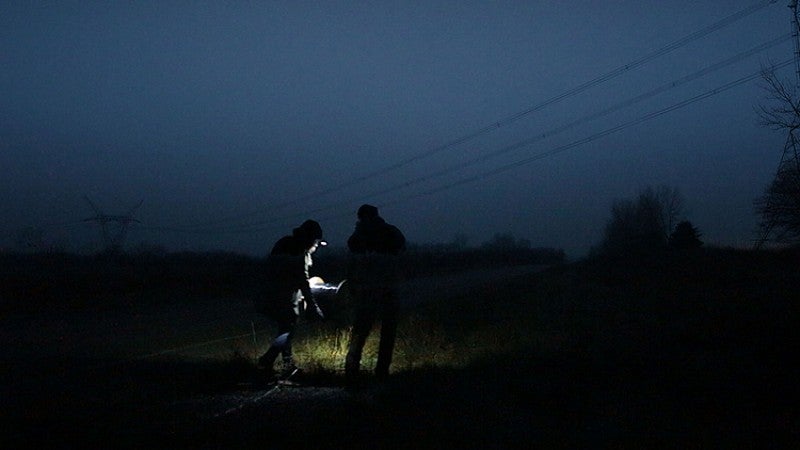 two people in the dark with flashlight in field under power lines