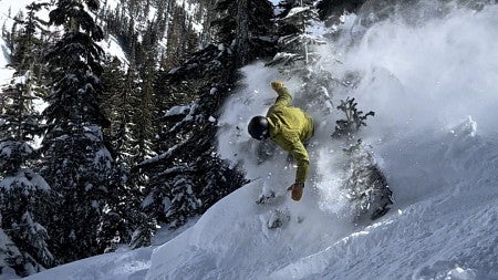 Trent snowboarding down a mountain, kicking up powder