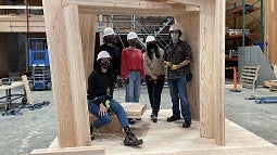 A team of students posing in a wooden structure they created.