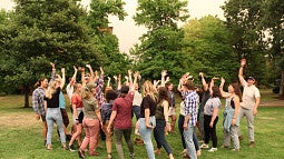 Photo of the latest RARE cohort outdoors with green trees and grass and arms raised in joy. 