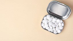 A tin of white mints is displayed on a peach-colored surface.