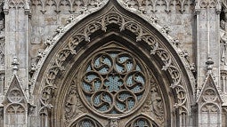 Photograph of Gothic architecture. Exterior view of a church window that show ornate, european-style stone features and glass.