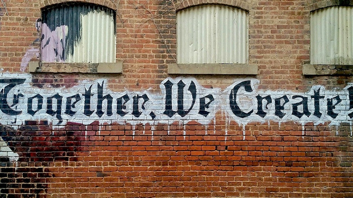 Graffiti that says Together We Create on brick wall