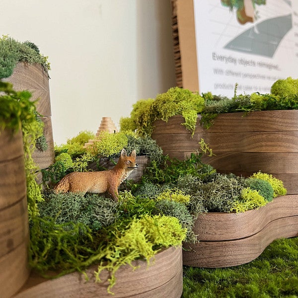 3D model of a multi-tiered structure made of wood covered in vegetation. Pictured is a plastic fox walking through the model.