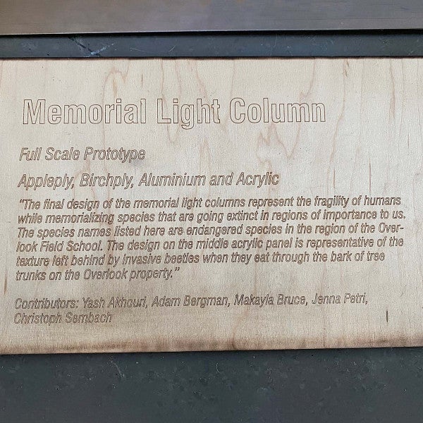 Plaque that reads, “Memorial Light Column; The final design of the memorial light columns represents the fragility of humans while memorializing species that are going extinct in regions importants to us. The species names listed here are endangered species in the region of the Overlook Field School. The design on the middle acrylic panel is representative of the texture left behind by invasive beetles when they eat through the bark of tree trunks on the Overlook Property.” 